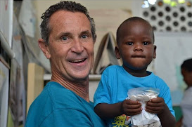 A smiling man holds Joseph, who is holding a packet of Previnex Super Vites, in rural southern Haiti