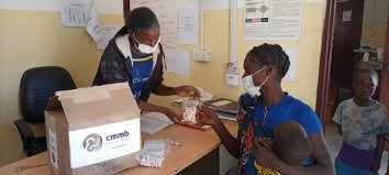 A community health assistant hands bottles of Previnex Super Vites to a mother holding her baby at a health post in Mwandi District, Zambia